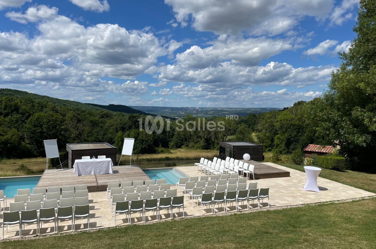 Chaises blanches disposées autour d'une piscine pour un événement en plein air avec vue sur une vallée boisée.