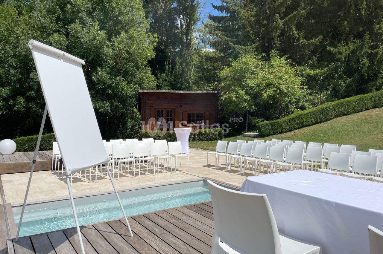 Chaises blanches disposées autour d'une piscine pour un événement en extérieur, avec un tableau de conférence et un chalet…