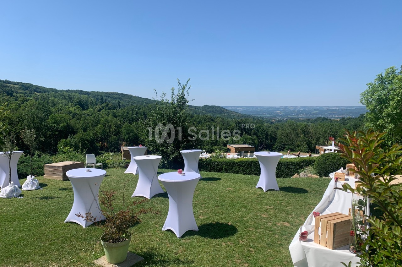 Tables hautes avec nappes blanches disposées sur une pelouse avec vue sur une vallée et des collines verdoyantes.