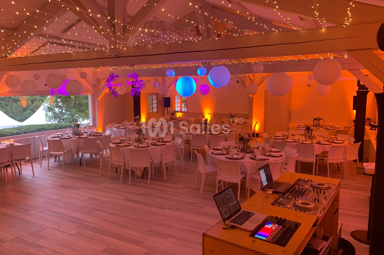 Salle de réception décorée avec des guirlandes lumineuses, des lampions suspendus et des tables dressées pour un événement.
