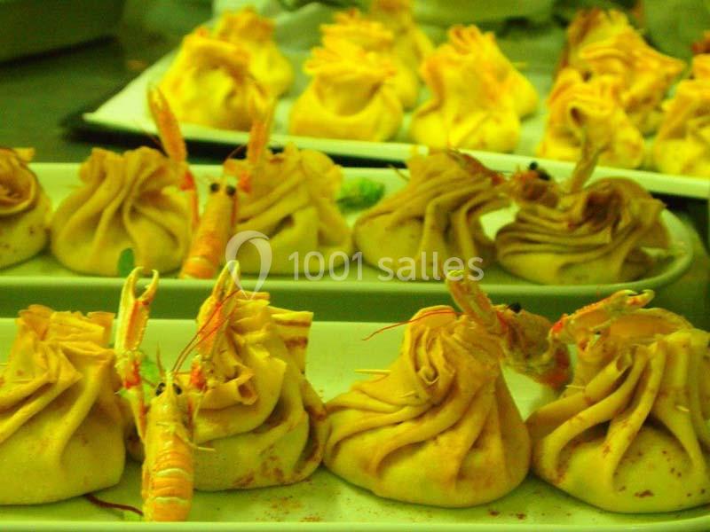 Des ravioles dorées garnies, décorées de crevettes, disposées sur des assiettes blanches.