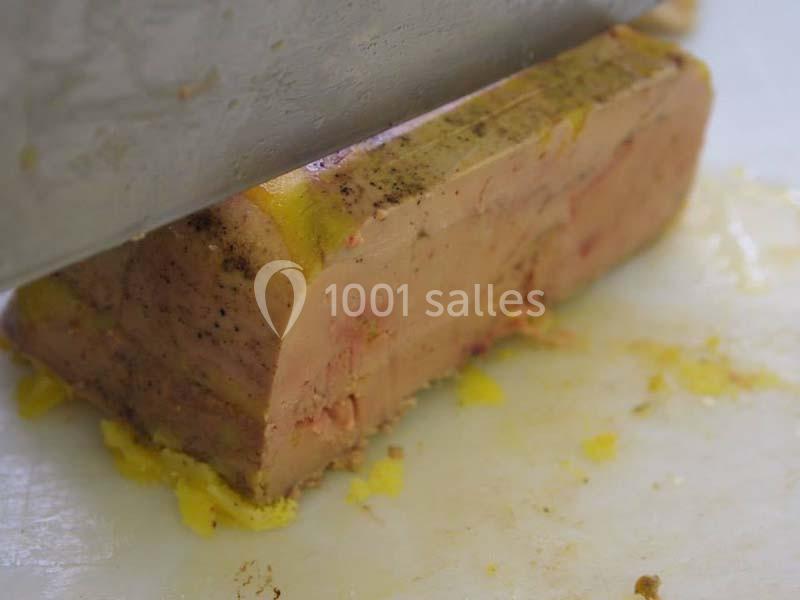 Bloc de foie gras coupé en tranches sur une planche, avec une couche de graisse jaune visible.