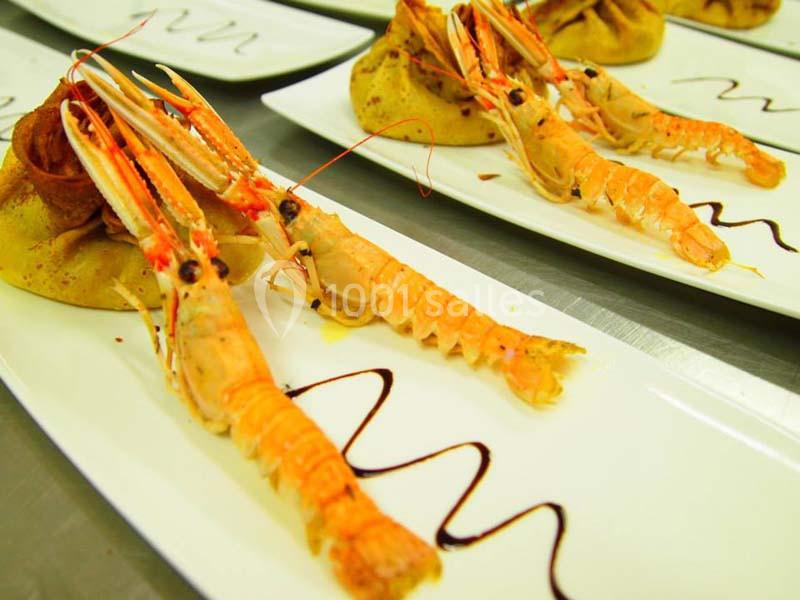 Assiette de langoustines dressées avec une sauce décorative et accompagnées de garnitures sur une table de service.
