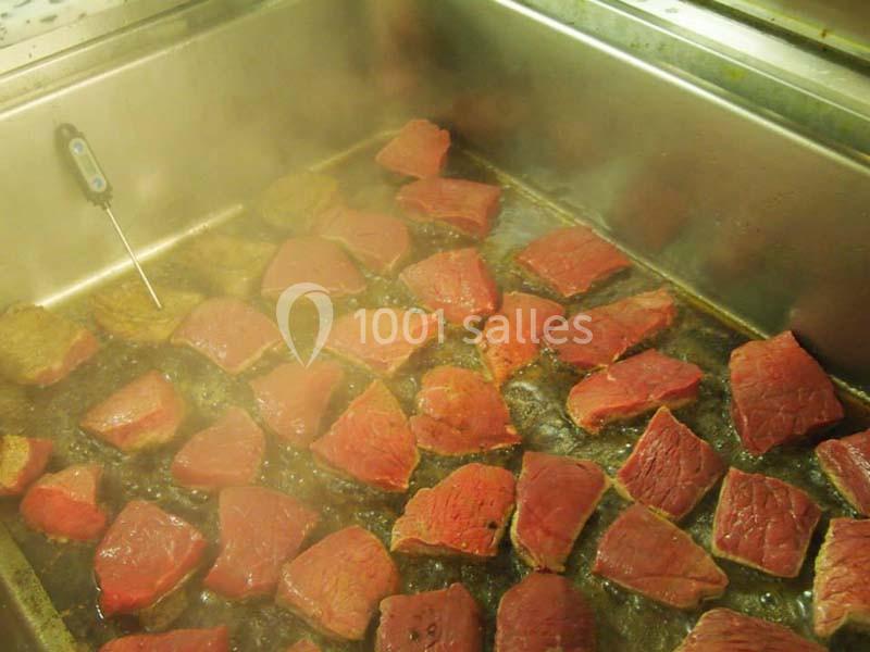 Morceaux de viande rouge en train de cuire dans un grand récipient métallique avec de la vapeur visible.