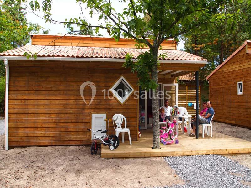 Famille assise sur la terrasse en bois d'un chalet en bois entouré d'arbres, avec des jouets d'enfants au sol.
