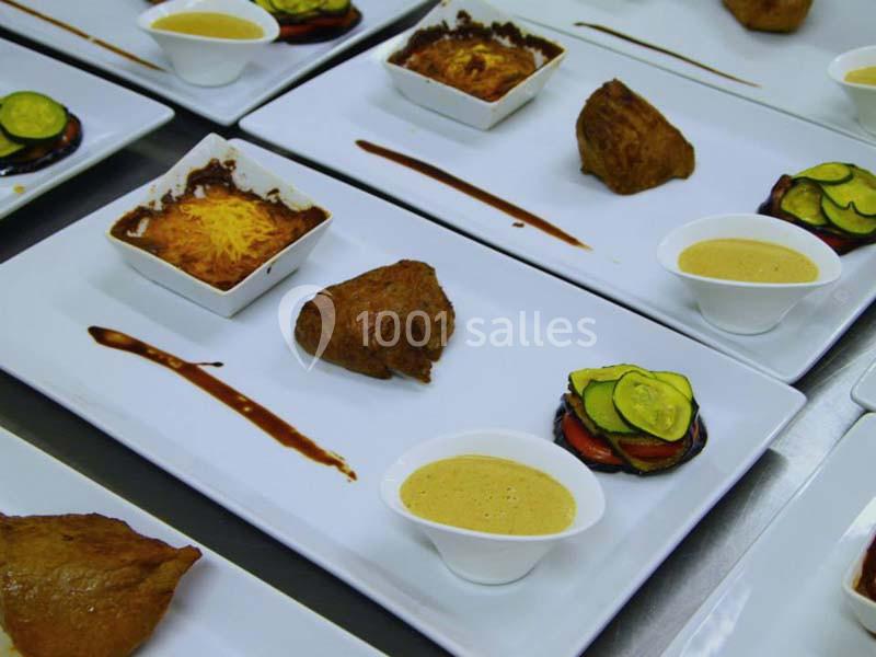 Assiettes gastronomiques avec viande, gratin, légumes en rondelles et sauce, présentées sur des plateaux blancs.