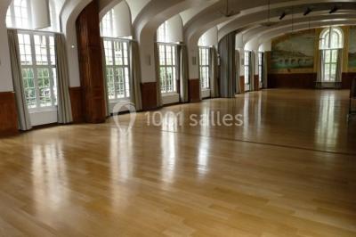 Banc en pierre au premier plan dans une allée bordée d'arbres, avec des promeneurs visibles au loin.