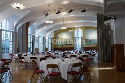 Banc en pierre au premier plan dans une allée bordée d'arbres, avec des promeneurs visibles au loin.