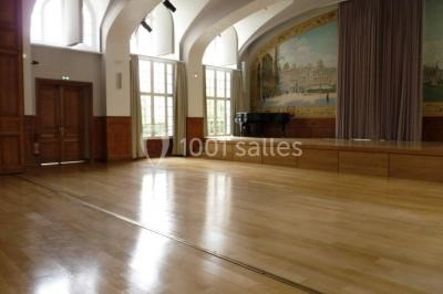 Banc en pierre au premier plan dans une allée bordée d'arbres, avec des promeneurs visibles au loin.