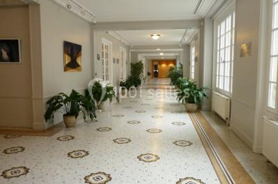 Banc en pierre au premier plan dans une allée bordée d'arbres, avec des promeneurs visibles au loin.