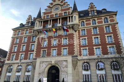 Banc en pierre au premier plan dans une allée bordée d'arbres, avec des promeneurs visibles au loin.