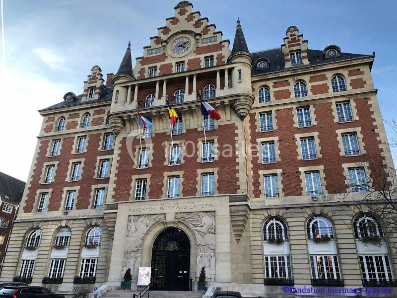 Façade d'un bâtiment en briques rouges avec des drapeaux européens, une horloge et des détails architecturaux classiques.