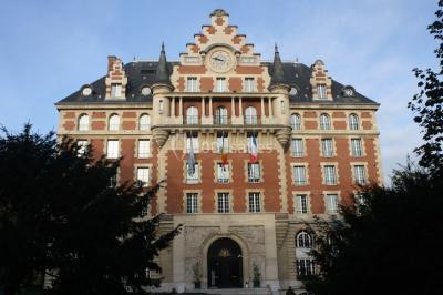Banc en pierre au premier plan dans une allée bordée d'arbres, avec des promeneurs visibles au loin.