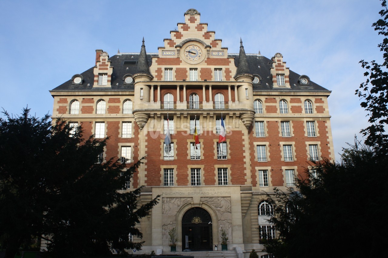 Façade d'un bâtiment en briques rouges et pierre avec une horloge centrale et des détails architecturaux ornés.