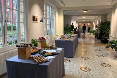 Banc en pierre au premier plan dans une allée bordée d'arbres, avec des promeneurs visibles au loin.