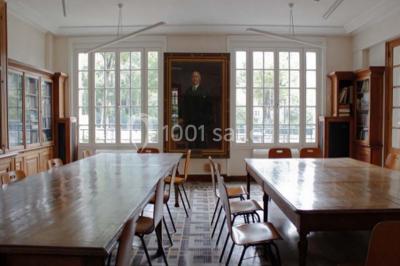 Banc en pierre au premier plan dans une allée bordée d'arbres, avec des promeneurs visibles au loin.