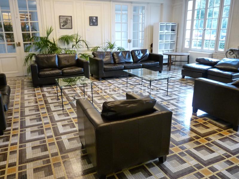 Salon lumineux avec canapés en cuir noir, tables basses en verre, plantes vertes et sol en carrelage géométrique.