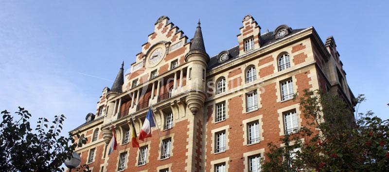 Façade d'un bâtiment en briques rouges avec des drapeaux français, des fenêtres alignées et un ciel dégagé.