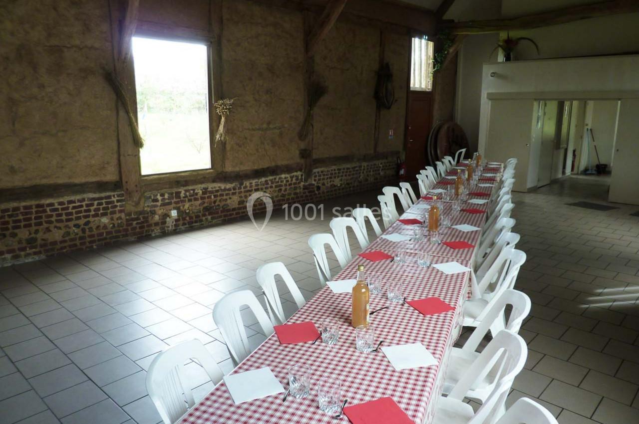 Grande table rectangulaire avec nappes à carreaux rouges et blancs, entourée de chaises blanches dans une salle rustique.