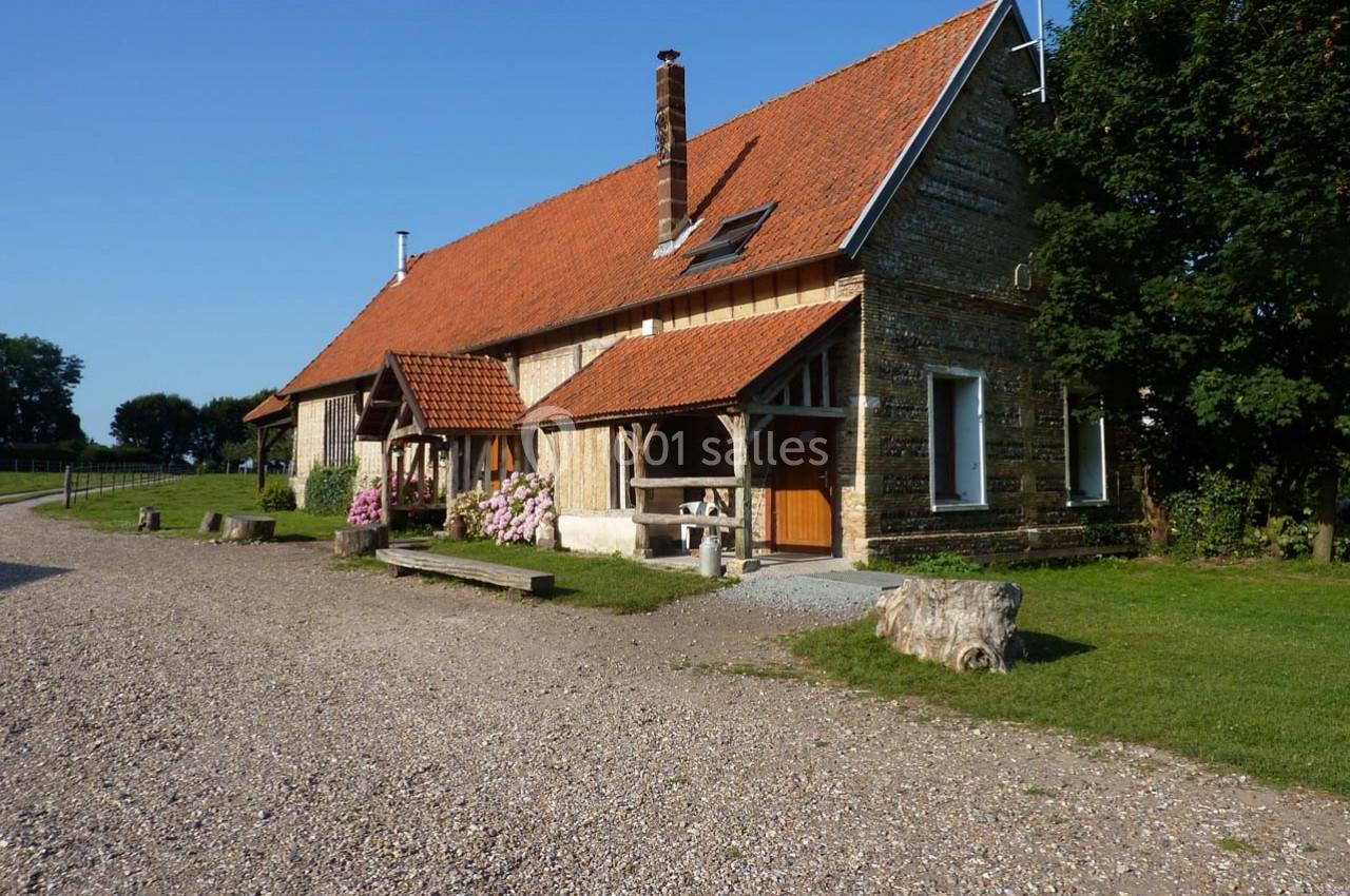 Maison en pierre avec toit en tuiles rouges, entourée de verdure et d'un chemin de gravier sous un ciel dégagé.