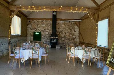 Salle rustique avec murs en pierre et poutres apparentes, aménagée avec tables hautes, canapés et décorations simples.