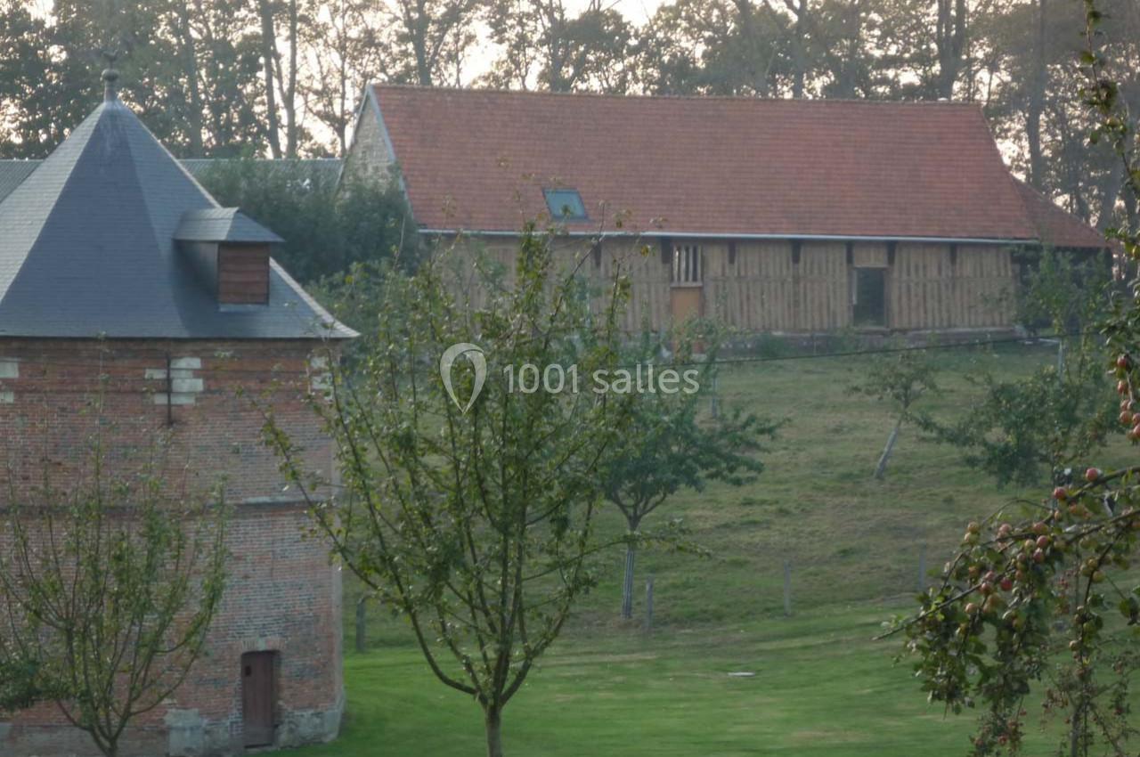 Bâtiments en briques et en bois dans un paysage rural avec arbres et pelouse au premier plan.
