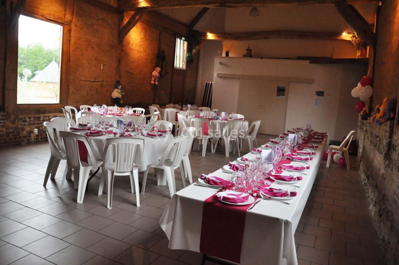 Salle décorée pour un repas festif avec des tables alignées, nappes blanches et accents rouges, chaises en plastique.