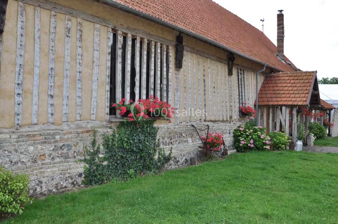 Façade d'une maison à colombages avec des fleurs en jardinières, un toit en tuiles et un jardin verdoyant.