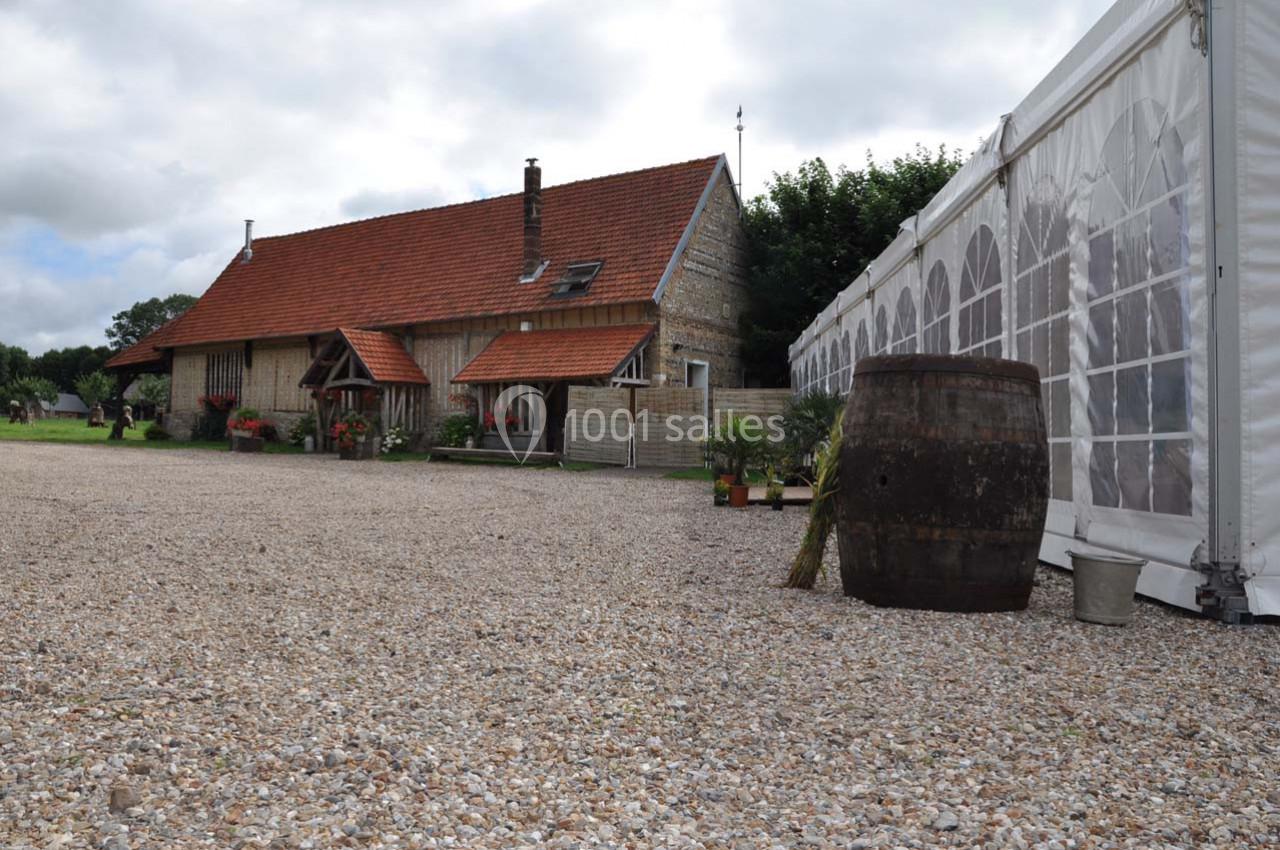 Maison en pierre avec toit en tuiles rouges, à côté d'une tente blanche et d'un tonneau sur une cour en gravier.