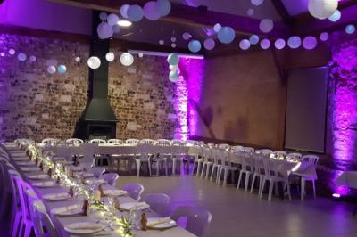 Salle rustique avec murs en pierre et poutres apparentes, aménagée avec tables hautes, canapés et décorations simples.