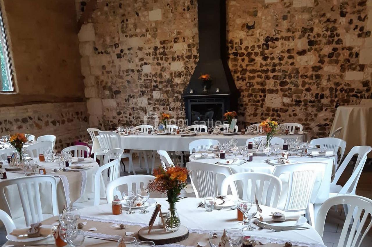 Salle décorée pour un événement avec des tables dressées, des chaises blanches et des fleurs en centre de table.