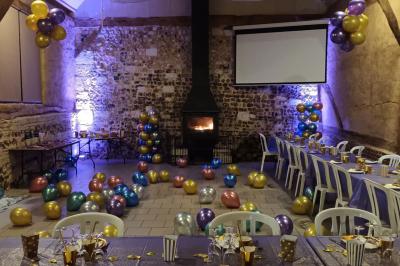 Salle rustique avec murs en pierre et poutres apparentes, aménagée avec tables hautes, canapés et décorations simples.