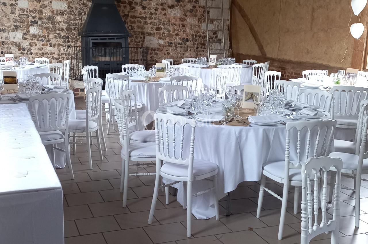 Salle de réception avec murs en pierre, tables rondes dressées de nappes blanches et chaises assorties.