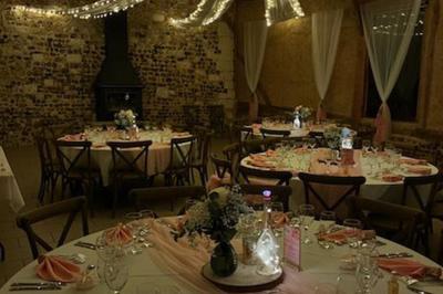 Salle rustique avec murs en pierre et poutres apparentes, aménagée avec tables hautes, canapés et décorations simples.