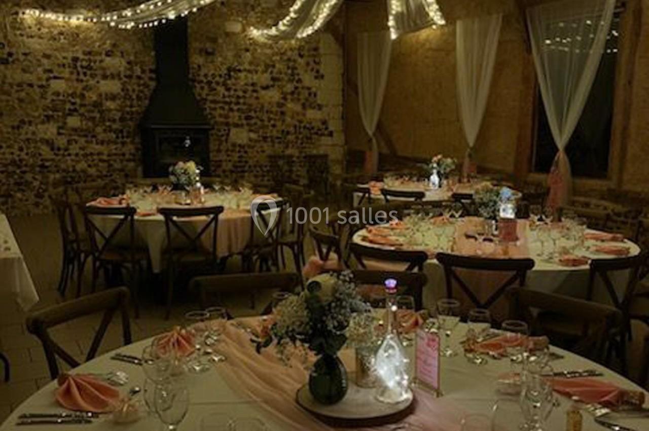 Salle de réception décorée avec des tables rondes, nappes blanches, serviettes roses et éclairage tamisé.