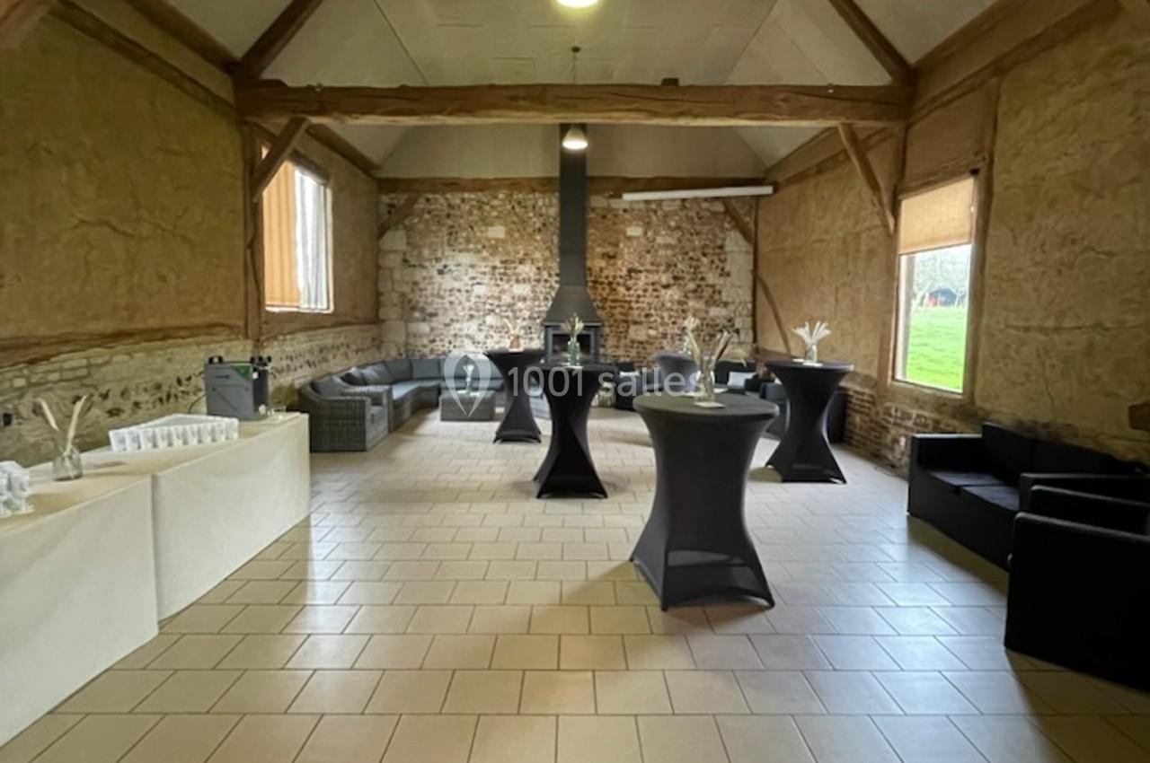 Salle rustique avec murs en pierre et poutres apparentes, aménagée avec tables hautes, canapés et décorations simples.