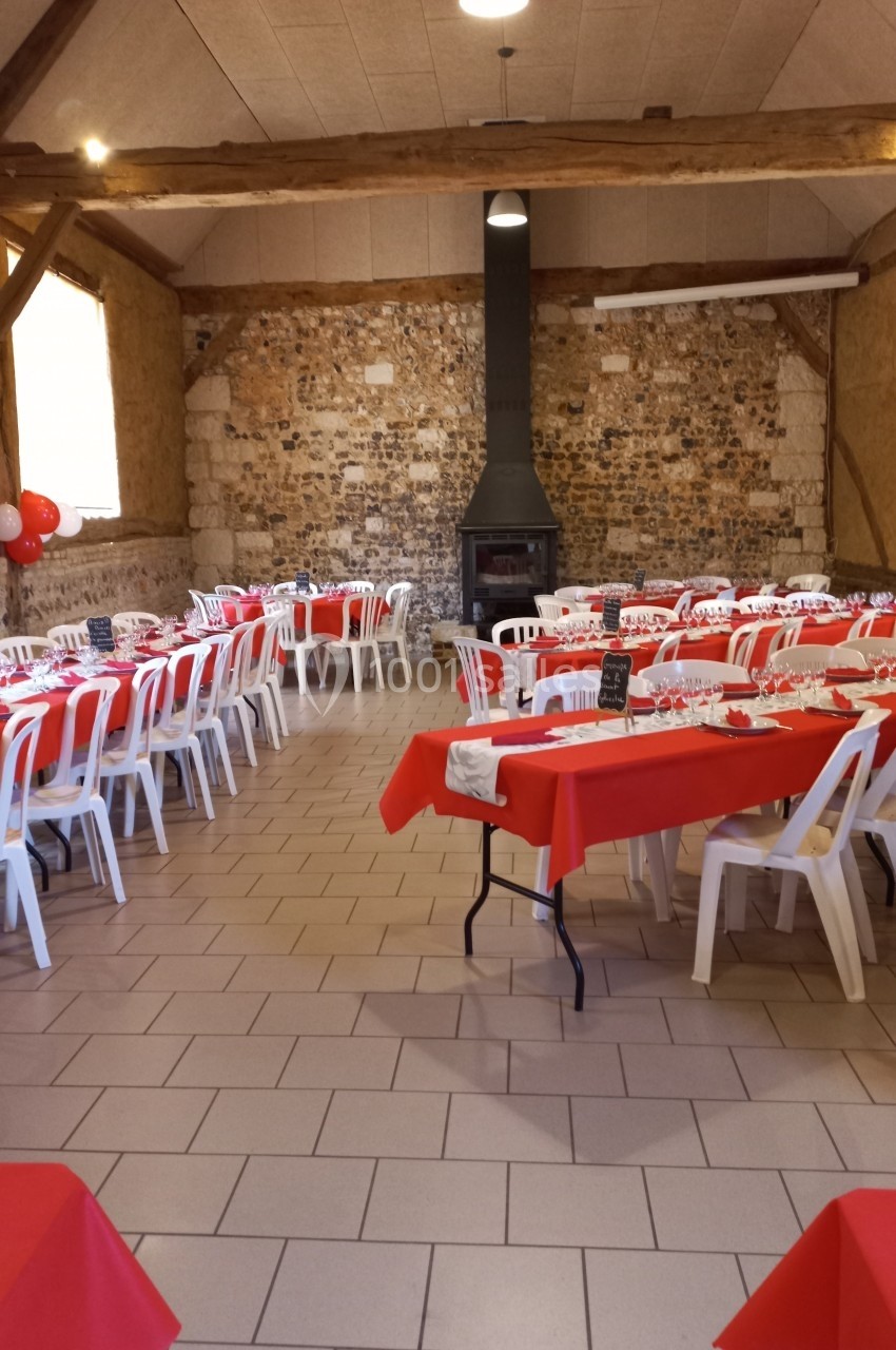 Location salle Montivilliers (Seine-Maritime) - Ferme d'Epaville #38 Salle décorée pour un événement, avec tables rouges dressées, chaises blanches et un poêle noir au fond.