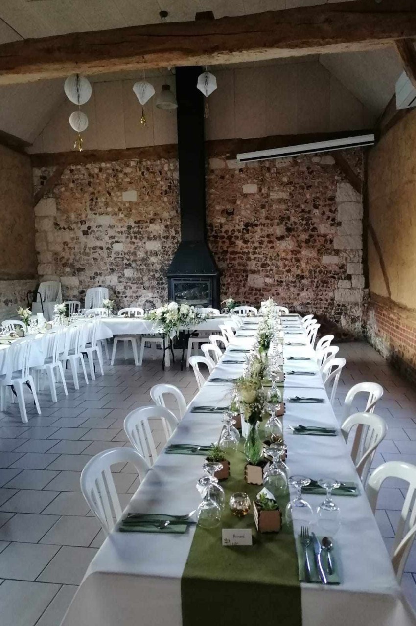 Location salle Montivilliers (Seine-Maritime) - Ferme d'Epaville #40 Salle rustique avec murs en pierre, tables dressées avec nappes blanches, chemins de table verts et décoration florale.