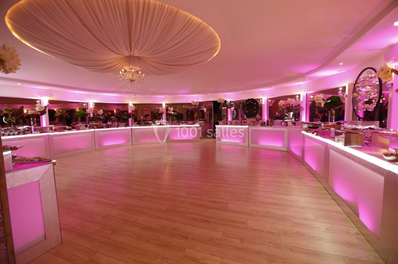 Salle de réception circulaire avec éclairage rose, tables de buffet alignées et plafond orné d'un drapé central.