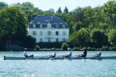 Des personnes discutent et se promènent le long d'une balustrade en fer forgé bordée de végétation, sous des arbres.