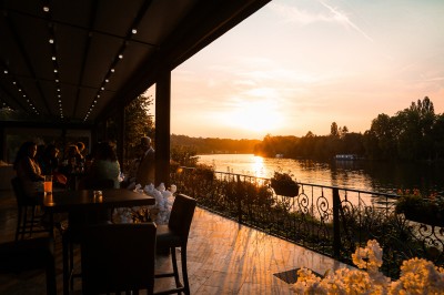 Des personnes discutent et se promènent le long d'une balustrade en fer forgé bordée de végétation, sous des arbres.