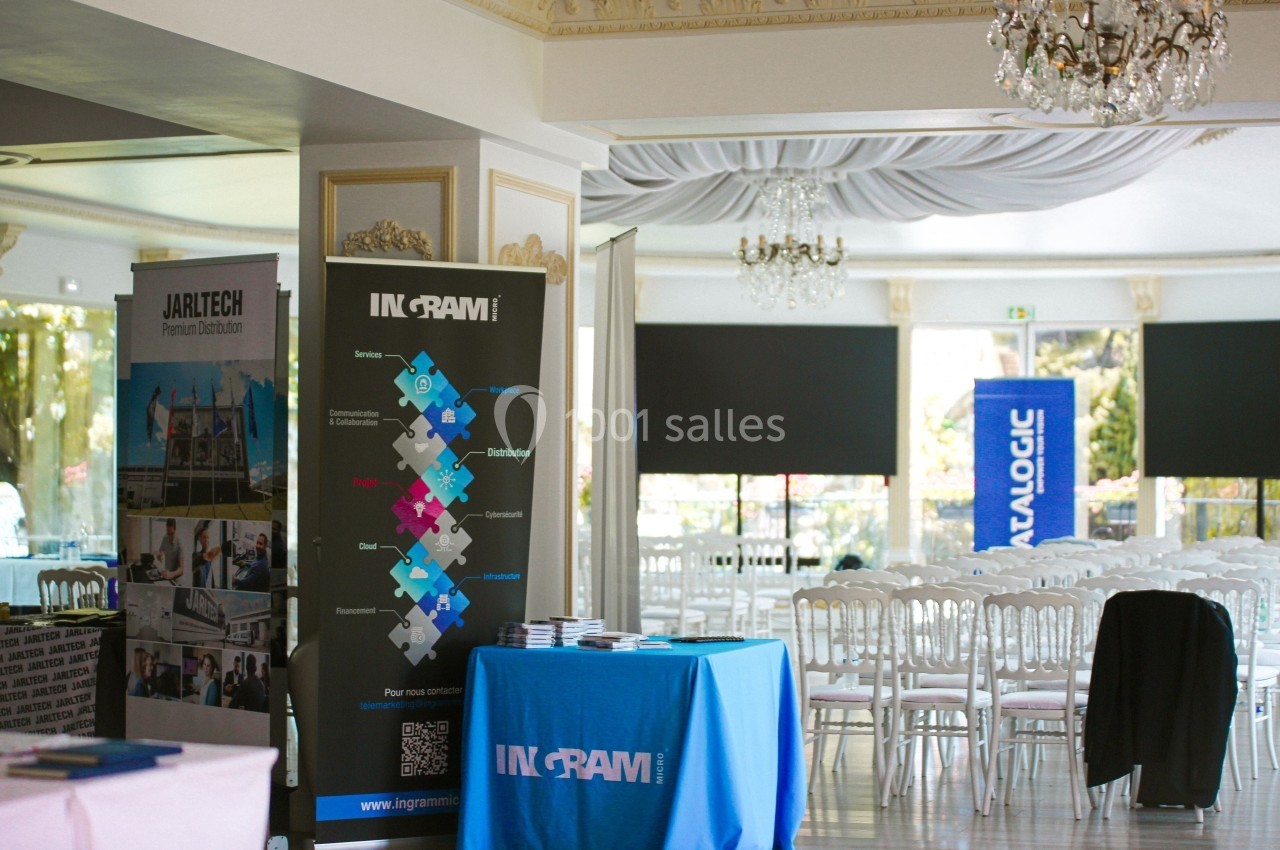 Salle lumineuse avec des stands promotionnels, des affiches et des tables recouvertes de nappes bleues, entourées de chaises…