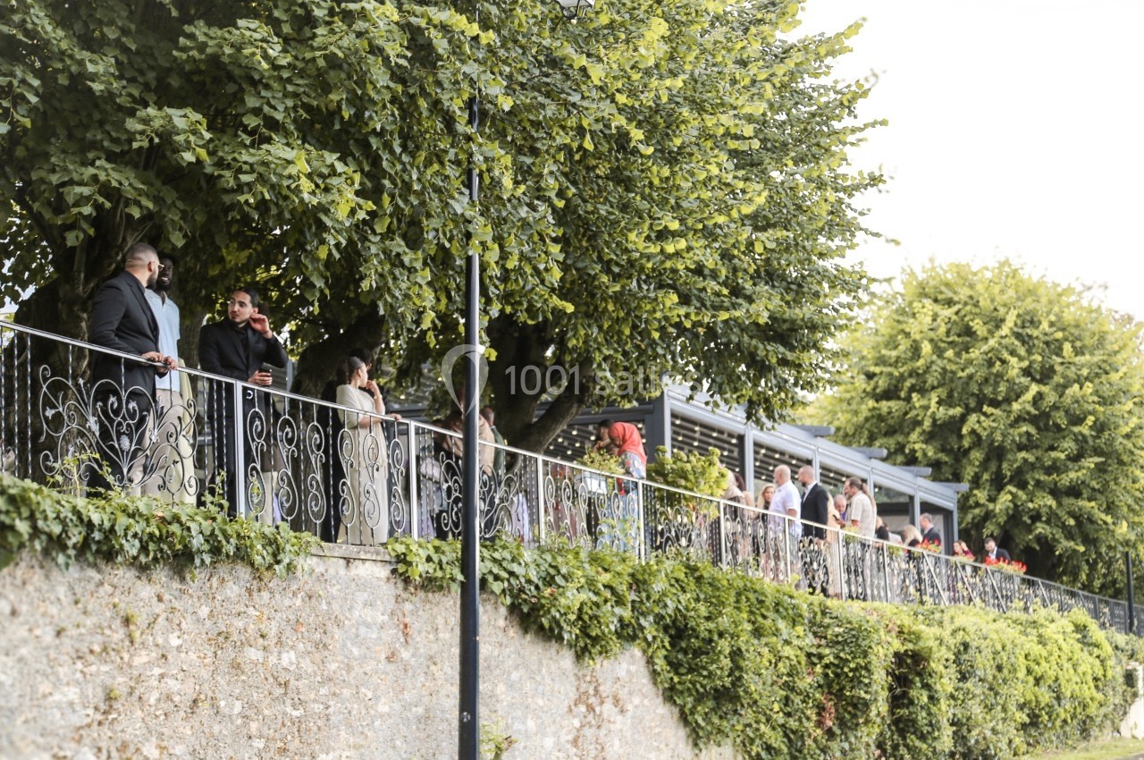 Des personnes discutent et se promènent le long d'une balustrade entourée de verdure et d'arbres.