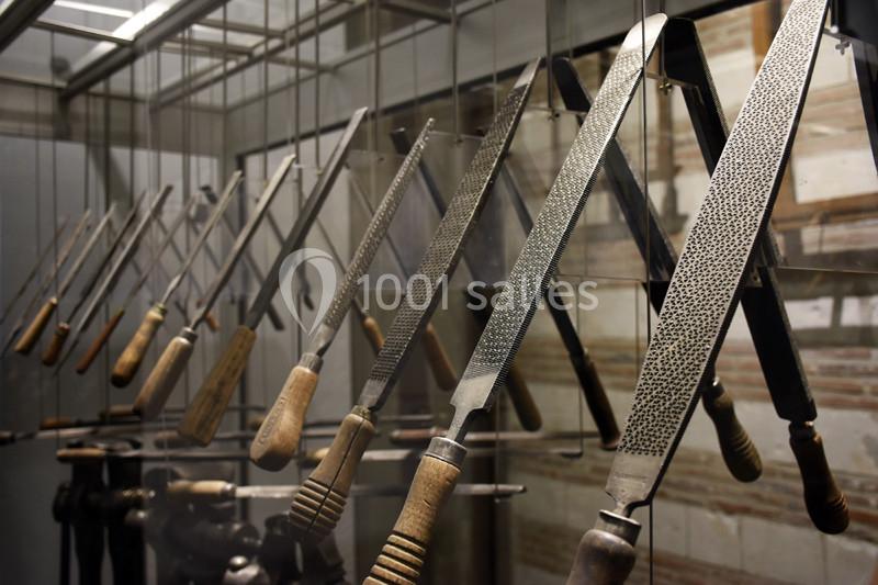 Rangée de limes métalliques suspendues avec des manches en bois dans un atelier ou une exposition artisanale.