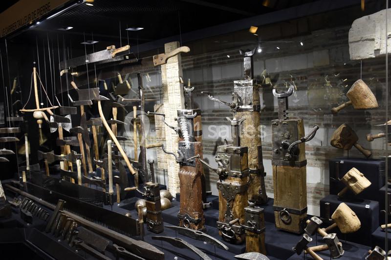 Vitrine exposant divers outils anciens en bois et métal, utilisés pour le travail du bois et de la pierre.