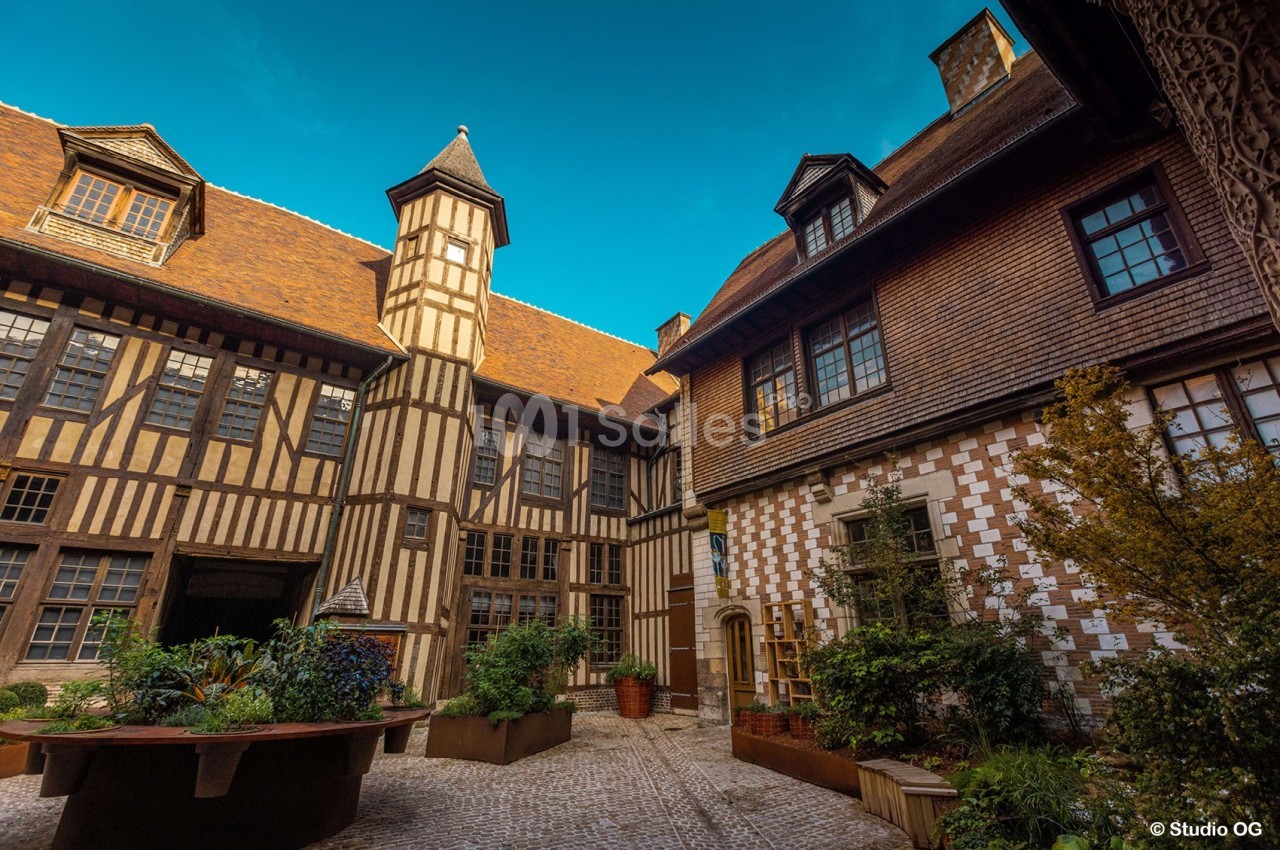 Cour intérieure d'un bâtiment à colombages avec des façades en bois et briques, entourée de végétation.
