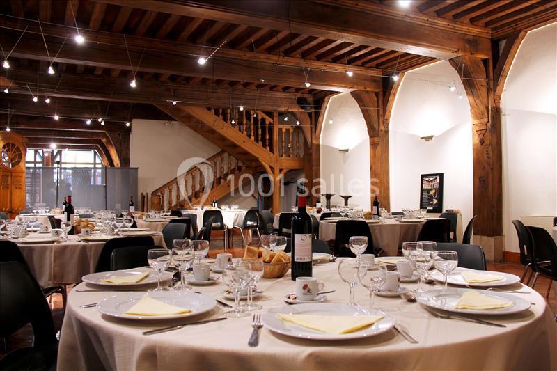 Salle de réception avec tables dressées, vaisselle élégante et poutres en bois apparentes.