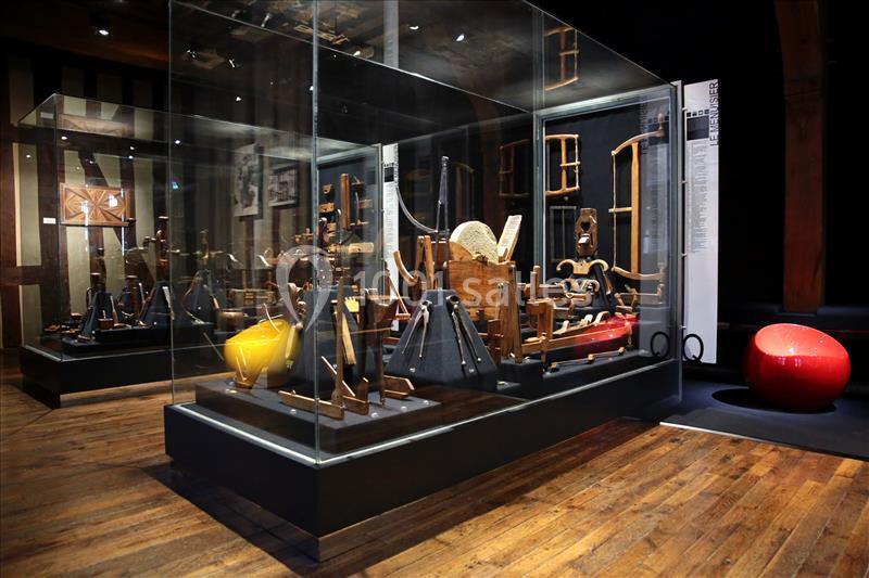 Exposition d'objets en bois dans une vitrine, présentés sur un sol en parquet dans un espace muséal sombre.
