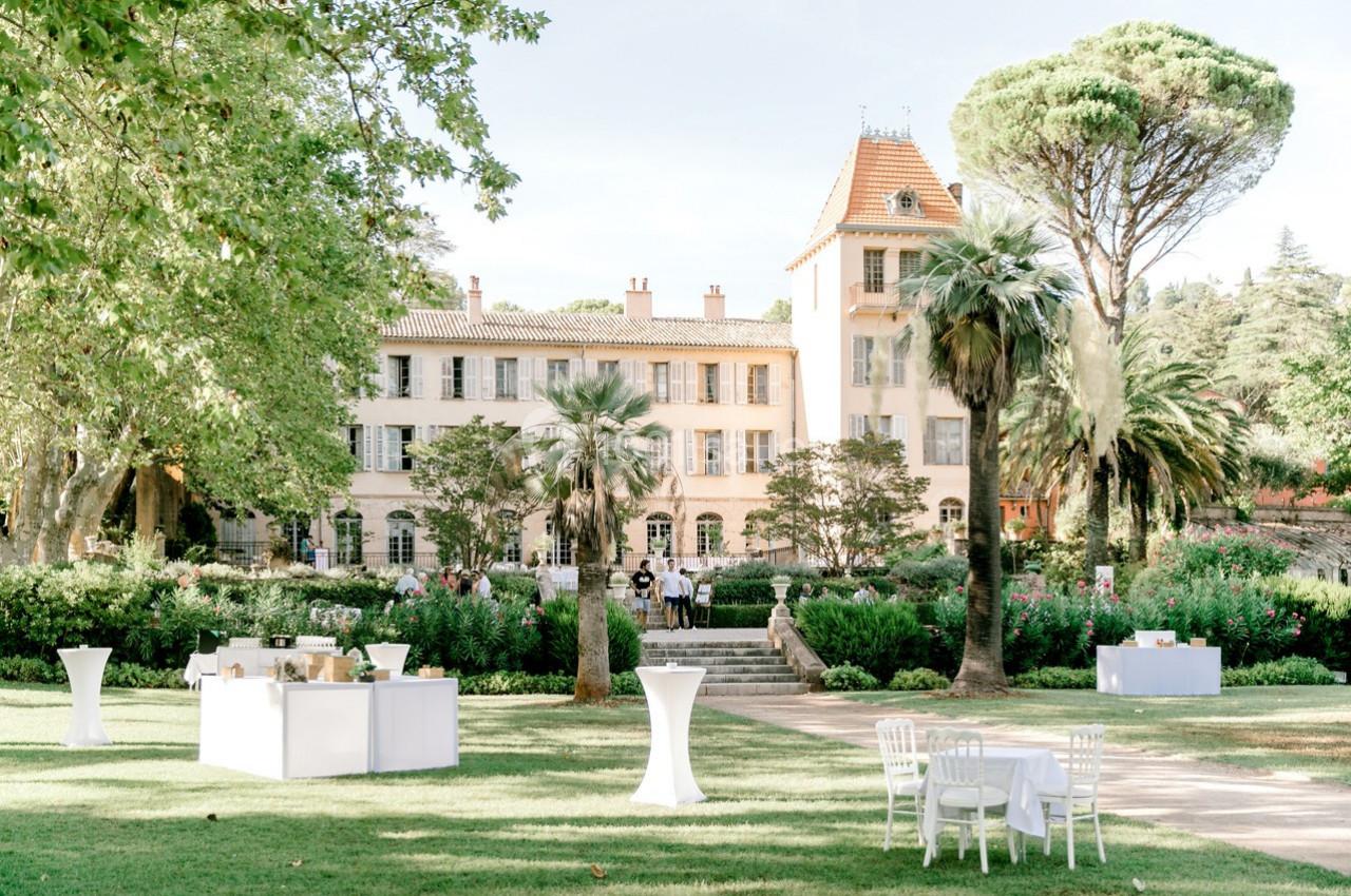 Jardin verdoyant avec tables dressées devant un grand bâtiment de style classique entouré d'arbres.