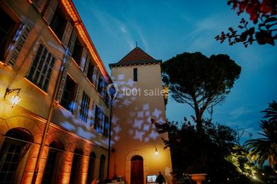 Allée bordée de palmiers éclairés, menant à une fontaine illuminée dans un jardin au crépuscule.